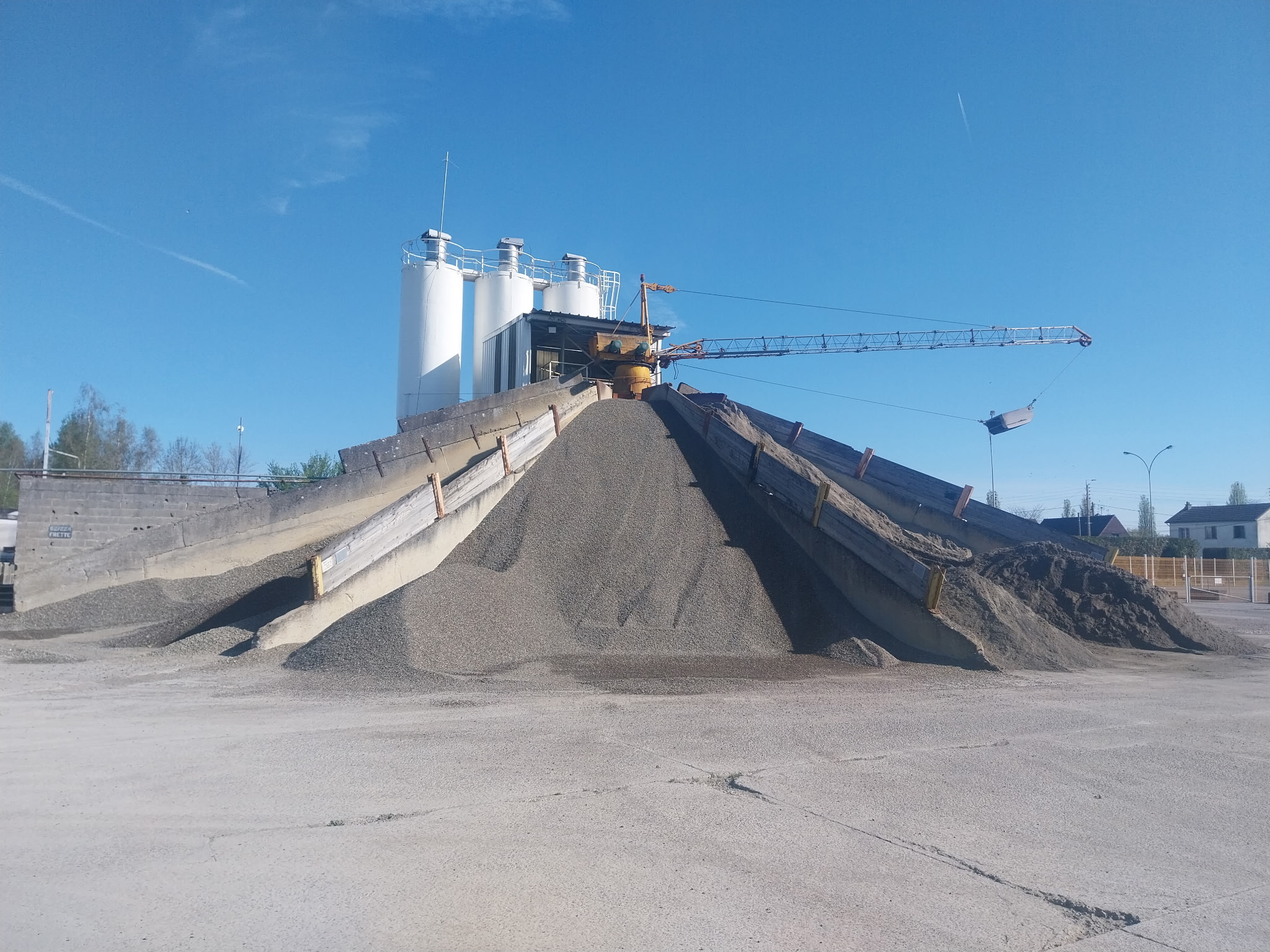 Une installation industrielle avec des silos blancs et de grandes piles de matériaux granulaires.