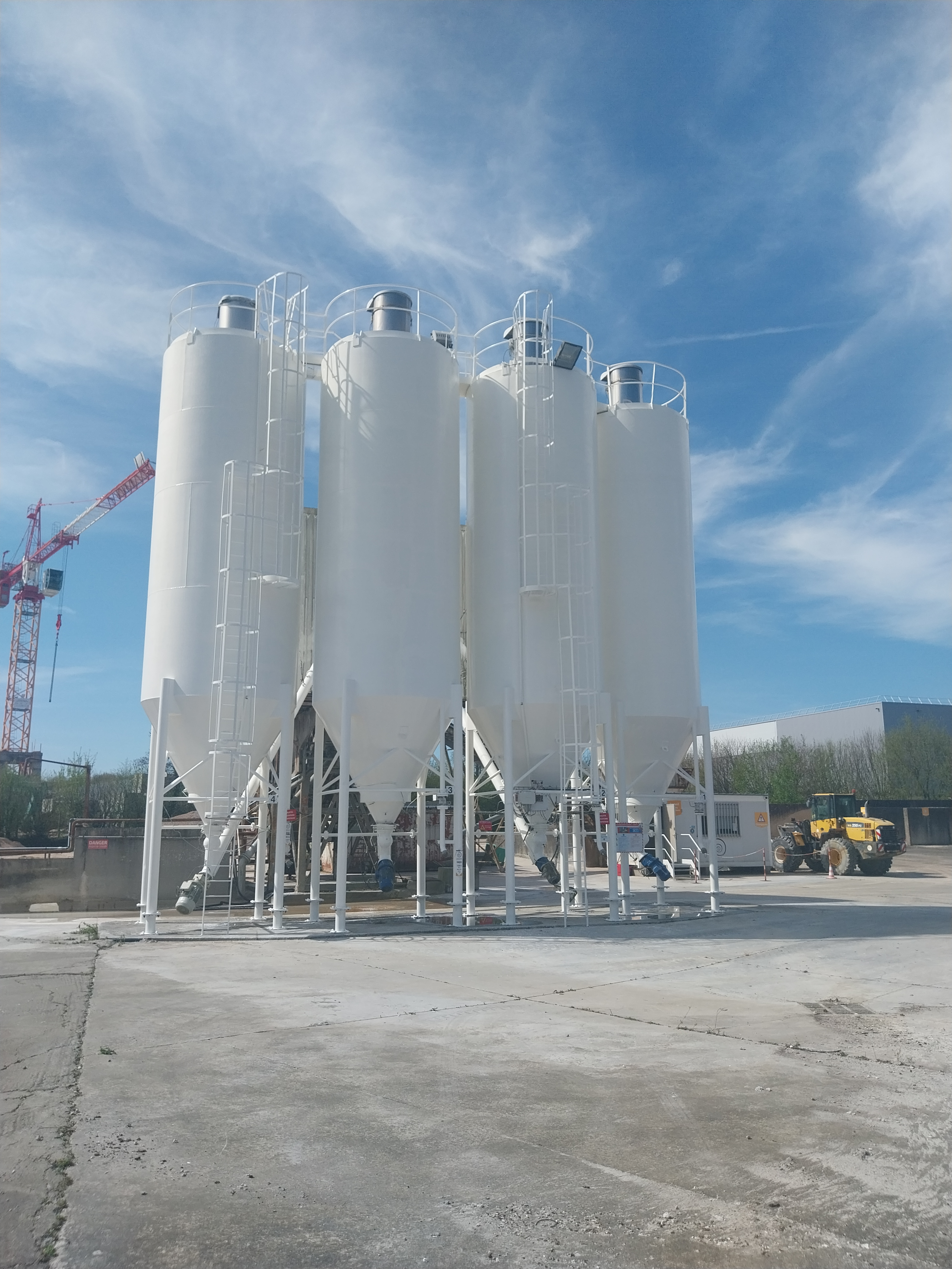 Silos blancs utilisés pour le stockage de matériaux de construction sur un site industriel.