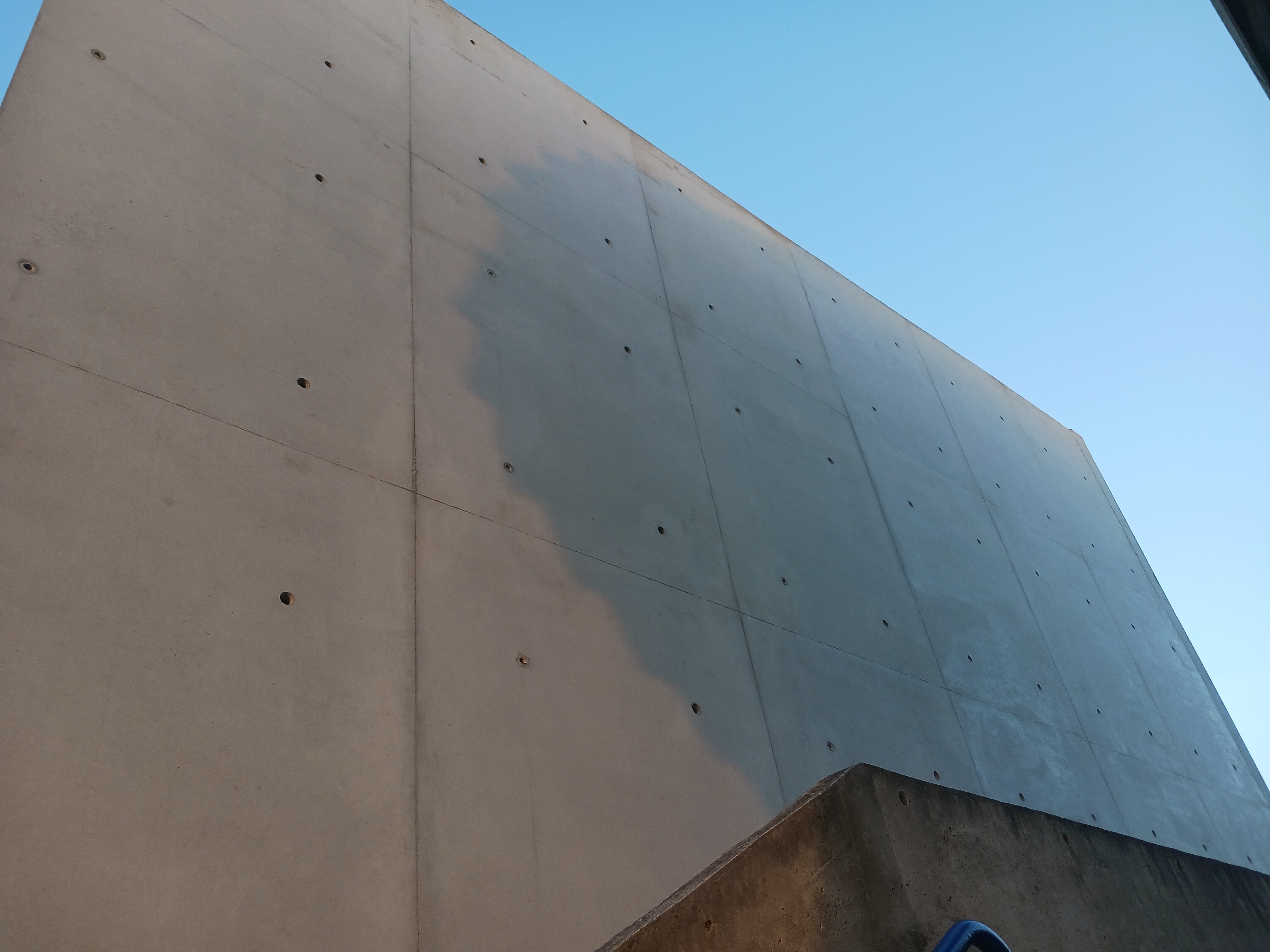 Mur en béton avec une partie légèrement ombrée, sous un ciel dégagé.