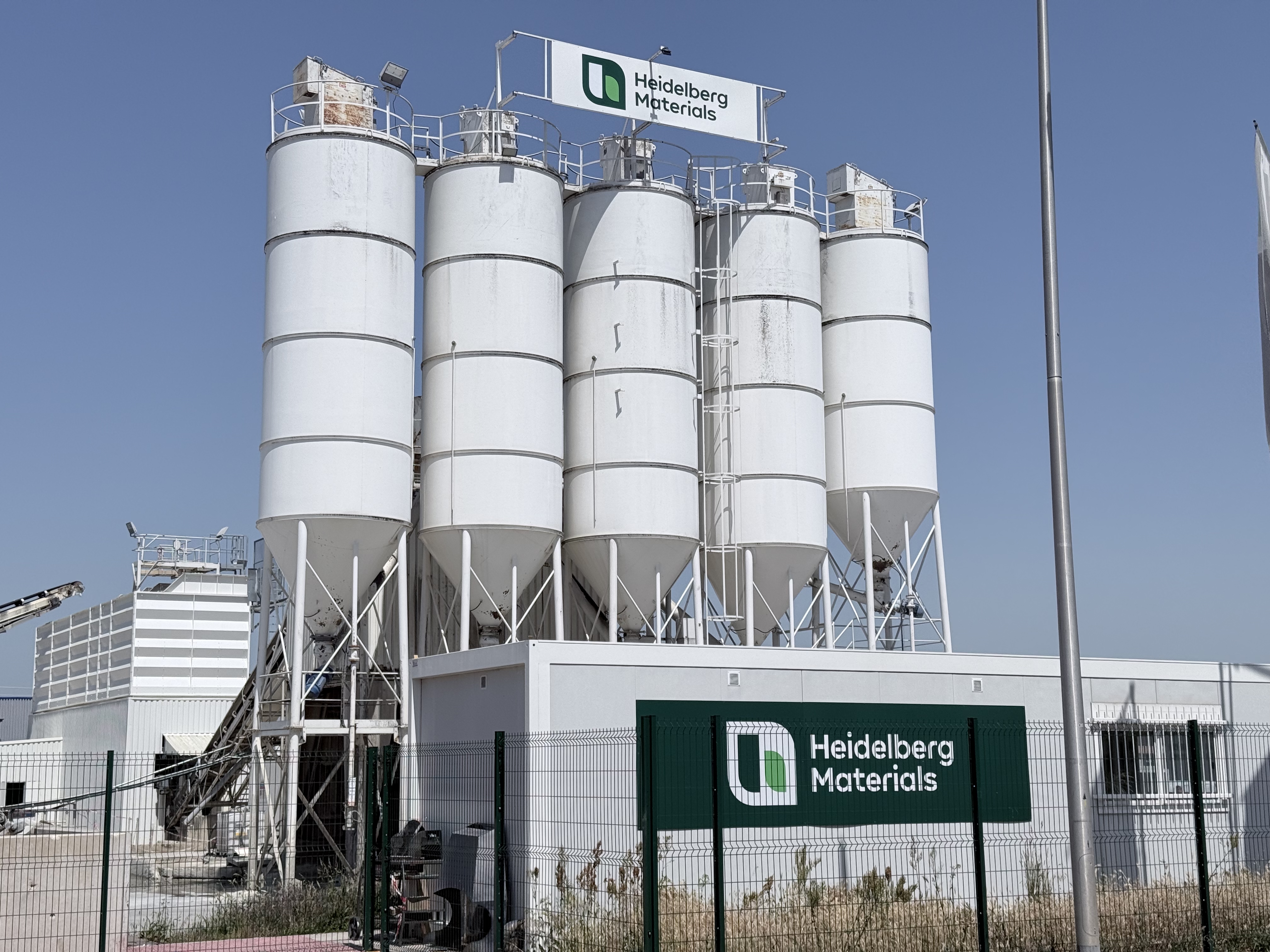 Des silos industriels blancs sur un site de Heidelberg Materials sous un ciel clair.